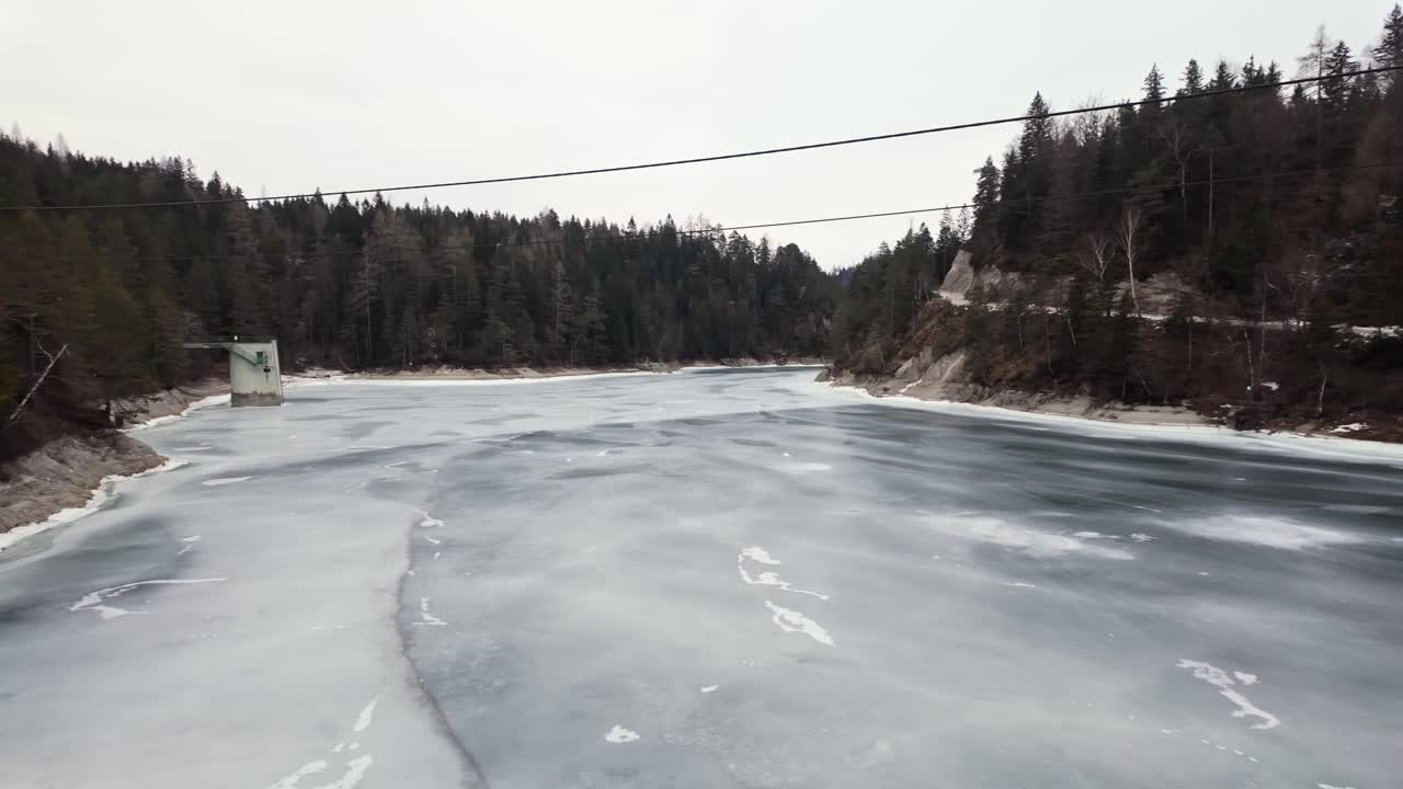 Pan shot of a frozen lake with ice, surrounded by trees and mountains. Capturing the serene winter landscape at Erlaufstausee, Styria, Austria.
