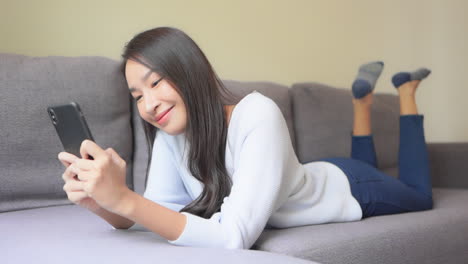 양손으로 스마트폰을 들고 집에서 휴식을 취하면서 스마트폰으로 채팅하는 아시아 여성