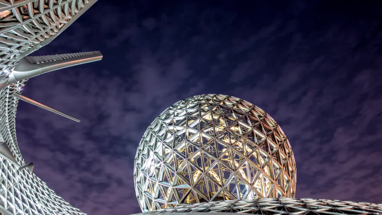 Futuristic metallic geodesic dome glowing under a cloudy night sky, creating a mesmerizing spectacle of modern architecture and innovative design
