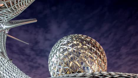 futuristic metallic geodesic dome glowing under a cloudy night sky, creating a mesmerizing spectacle of modern architecture and innovative design
