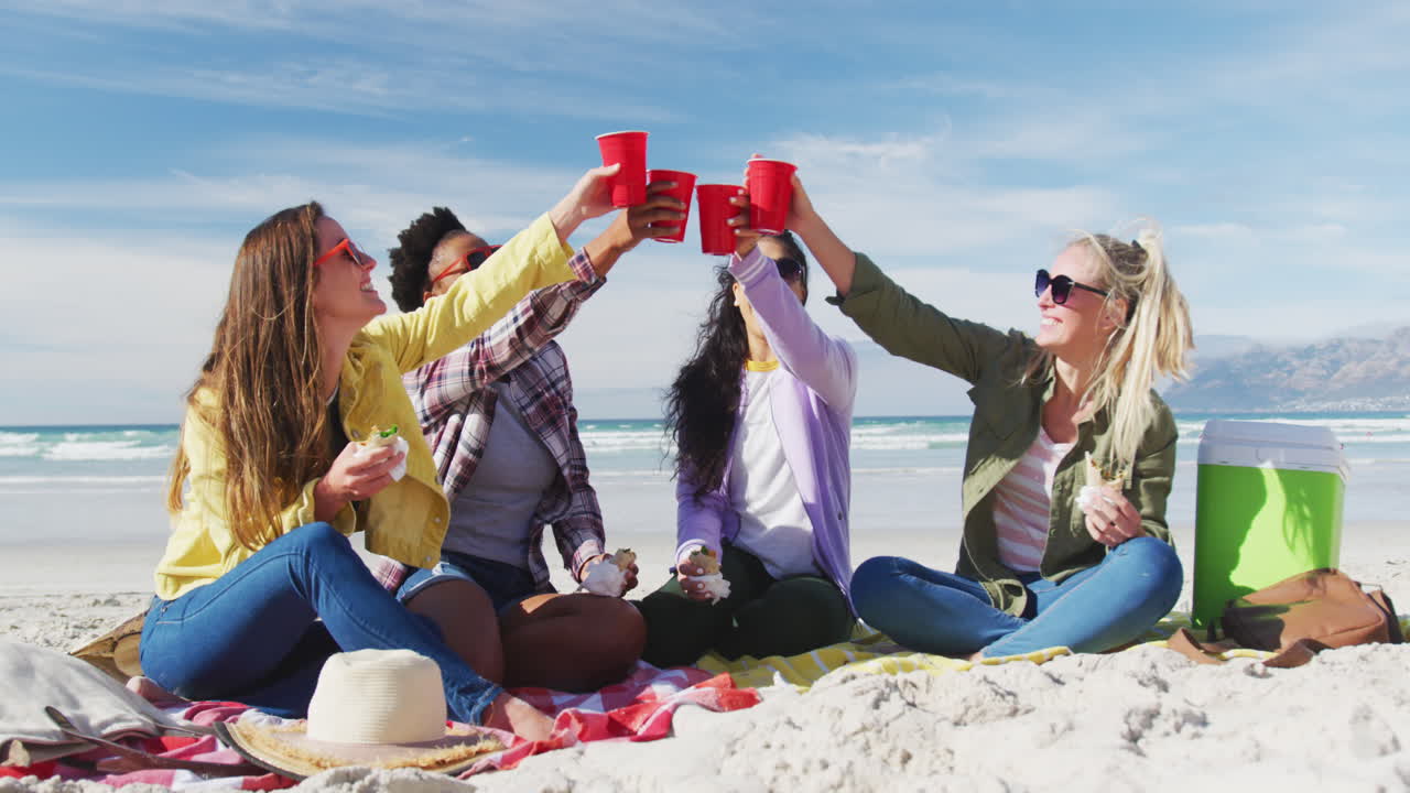 un grupo feliz de amigas diversas divirtiéndose, haciendo picnic en la playa