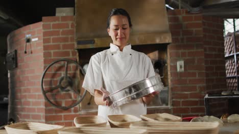 animation of of happy asian female baker sieving flour on board