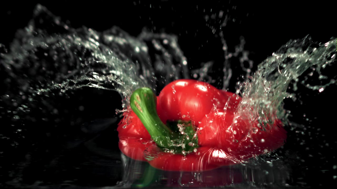Červená paprika padající do vody s cákancem ve zpomaleném záběru