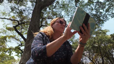 tilt up adult caucasian woman reading book under tree. nature park. asmr relax concept