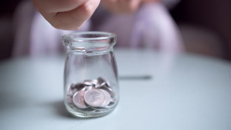 hand is putting a coin into glass jar on a blue background