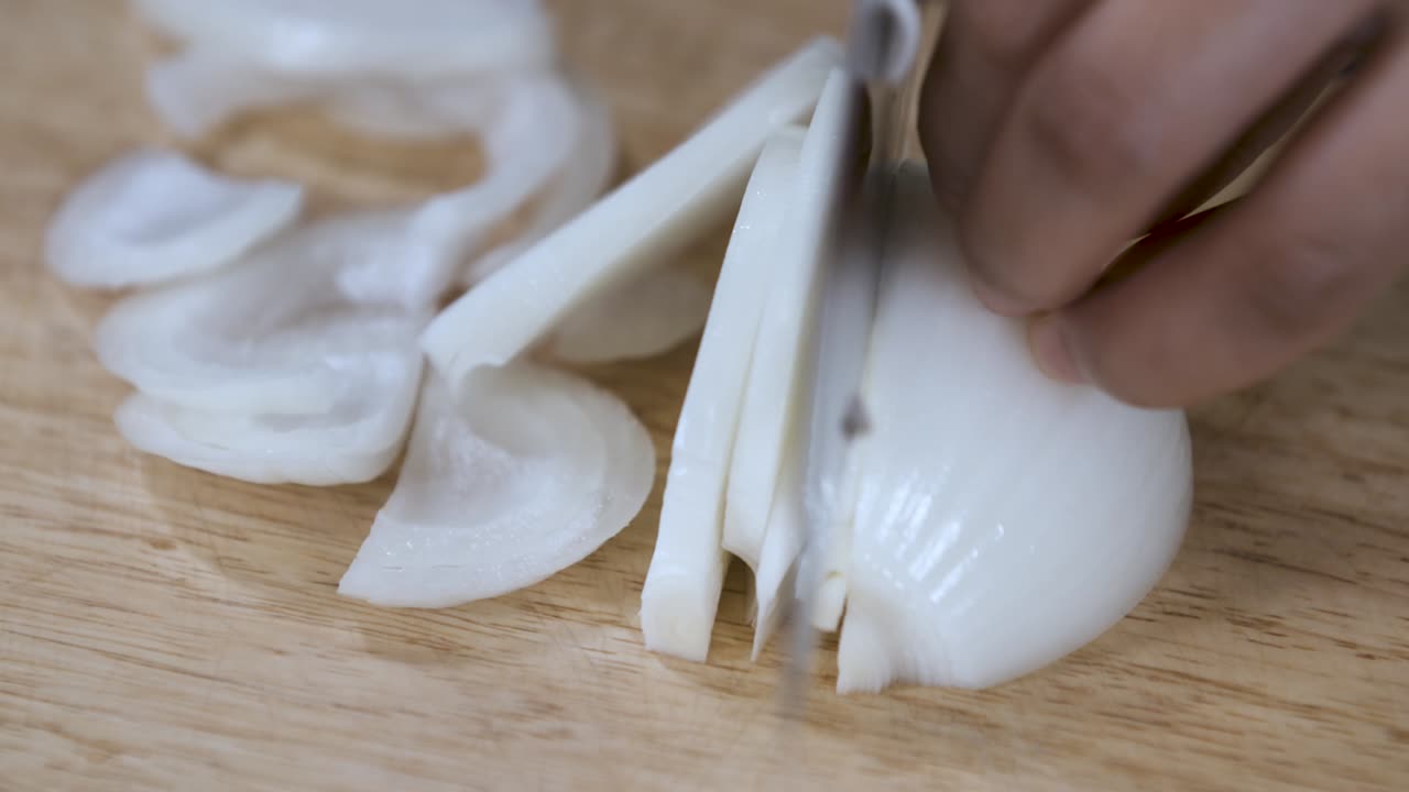 Cutting a White Onion into Slices with Knife on Wooden Chopping Board