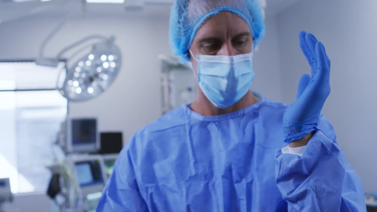 cirujano caucásico con máscara facial, gorra quirúrgica poniendo guantes en el quirófano