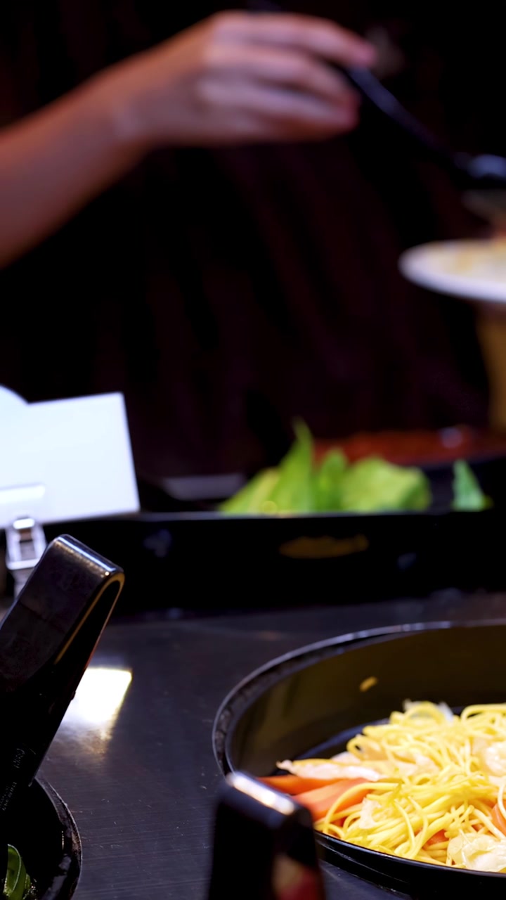 Close-up of woman scooping noodles and vegetables at bright self-service salad buffet station