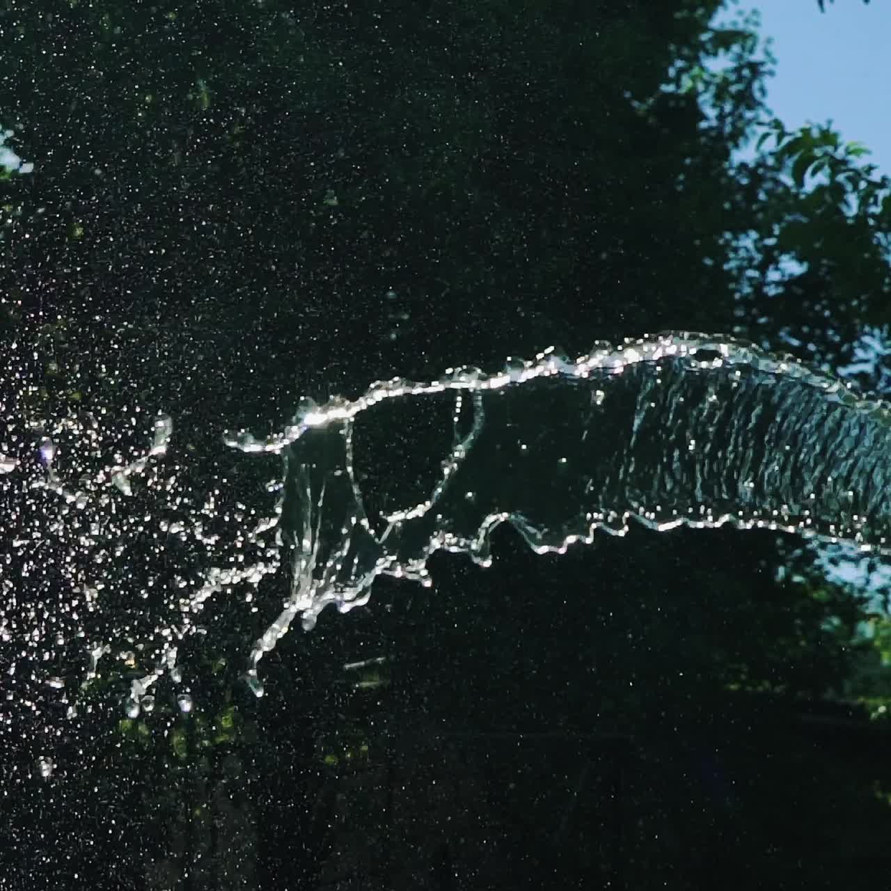 human's hands are holding a hose with water in the yard. Water are flowing by stream on the background of garden. Slow motion