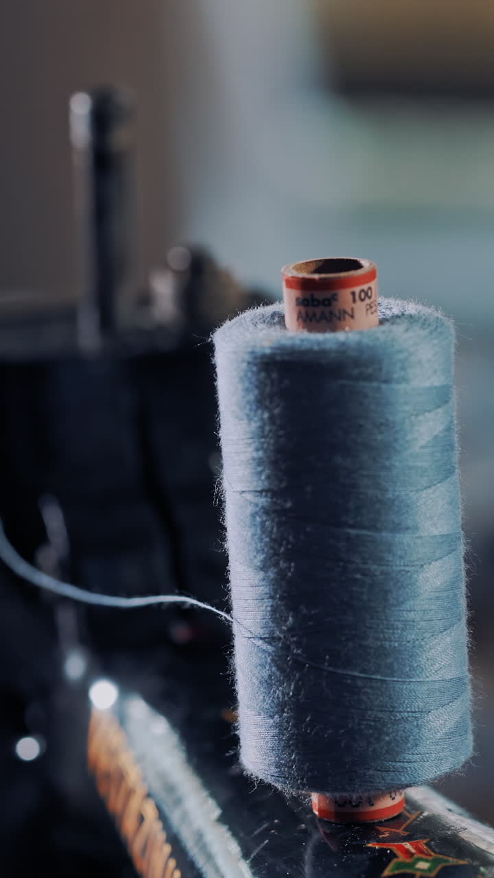 Close-up of a bobbin of blue thread on the sewing machine spinning. Cotton reel spinning on sewing machine for making dress in atelier. Slow motion. Vertical video
