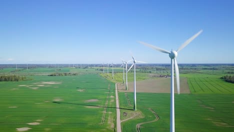 風力發電廠的風力輪在風力發電場中產生可再生能源的空中景色,陽光明<unk>的春天,綠色農業穀物田,鄉村道路上空低空飛行,無人機拖車向右移動