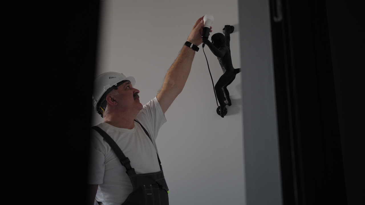 The electrician screws in the light bulb and it lights up. Electrician inserts and checks the operation of the light bulb in the luminaire