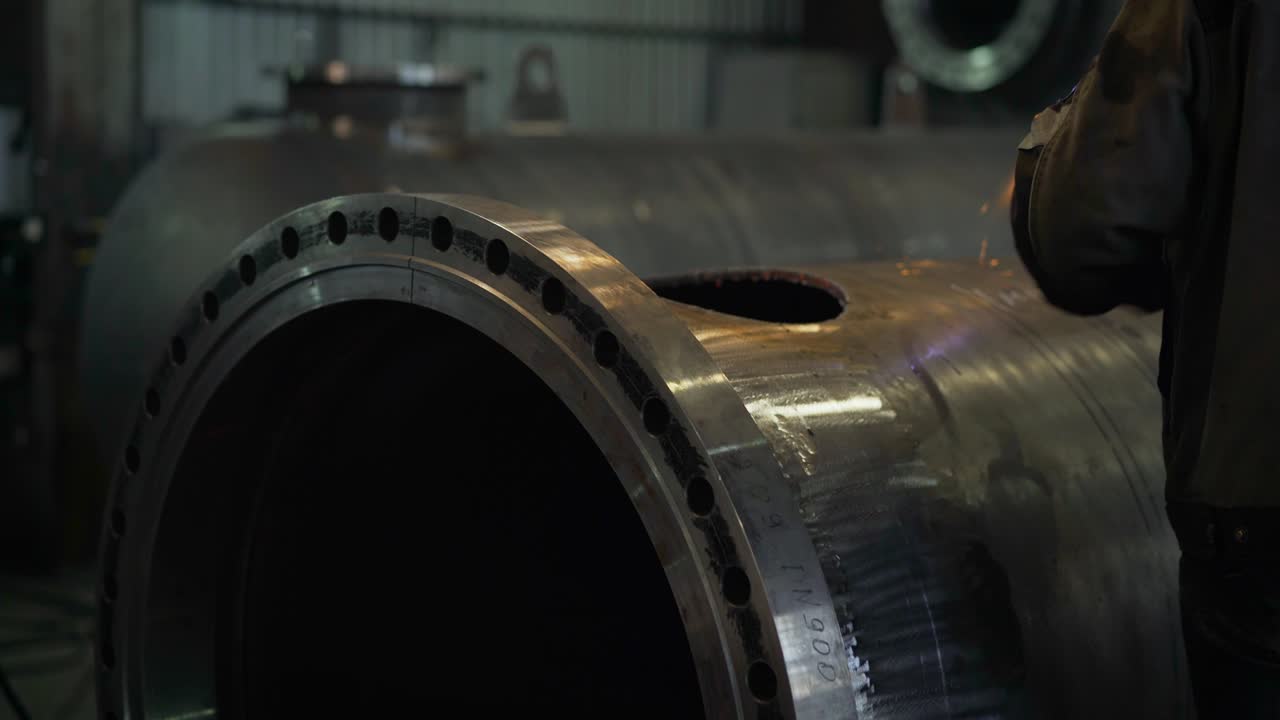 Un operaio dell'industria pesante taglia un'enorme tubazione. Una smerigliatrice da lavoro taglia il metallo in fabbrica