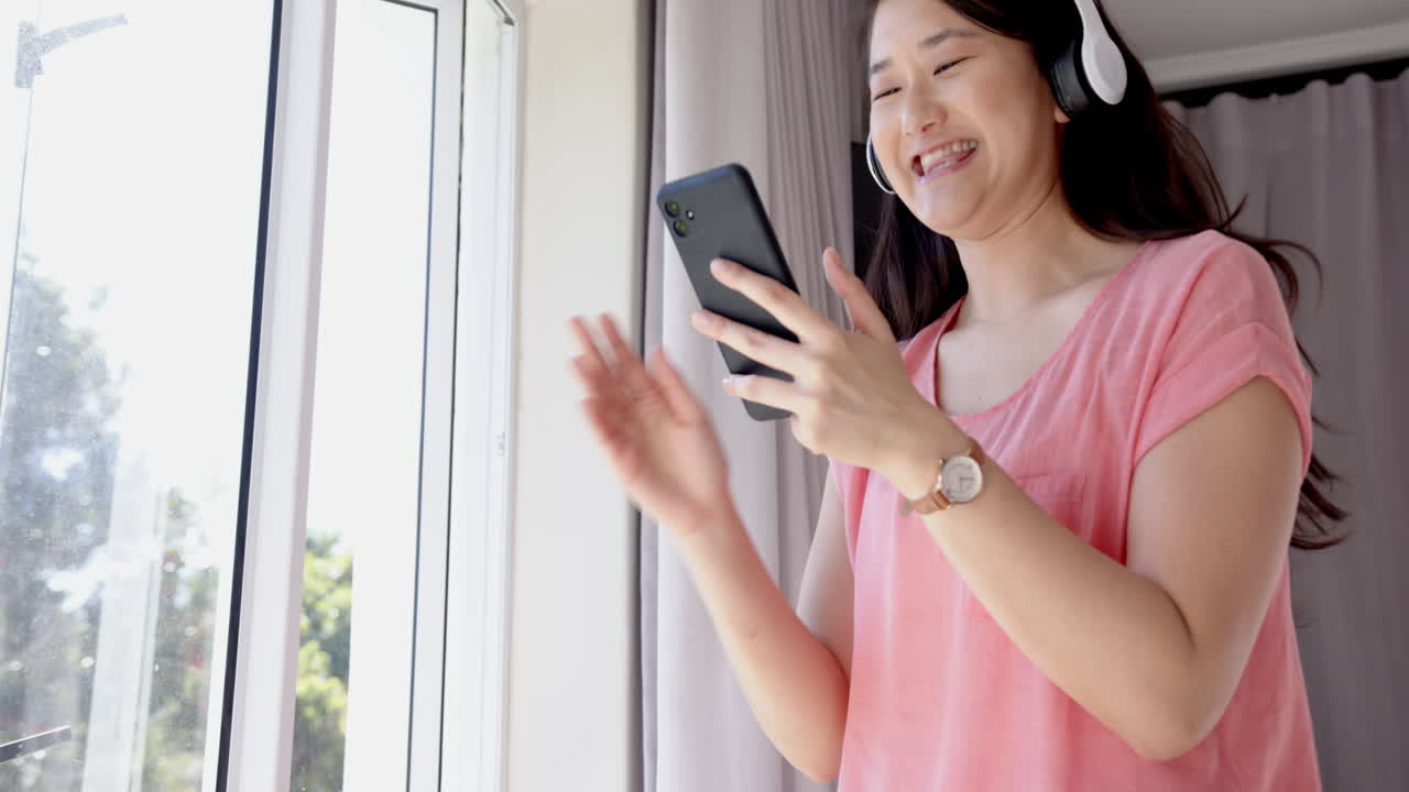 Wearing headphones, woman holding smartphone and looking out window, enjoying music