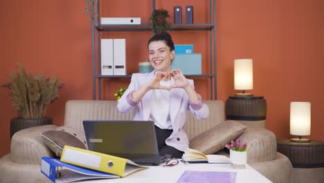 home office worker young woman makes heart symbol looking at camera.