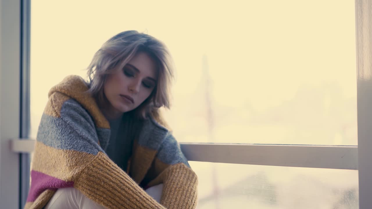 cu giovane ragazza carina si siede sullo sfondo delle finestre pensierosamente