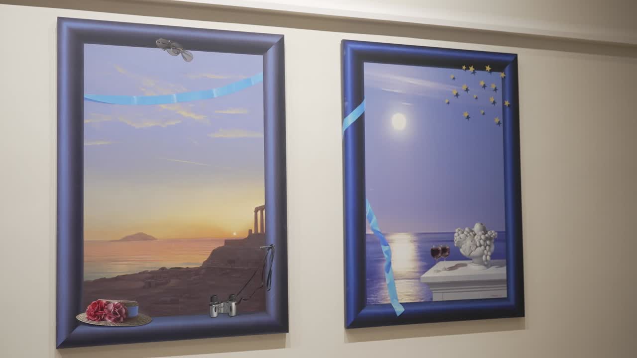 Due cornici d'arte appese a una parete, che mostrano vedute costiere con tramonti. La prima cornice raffigura un paesaggio di rovine antiche e la seconda mostra una spiaggia illuminata dalla luna. Sono presenti oggetti decorativi.