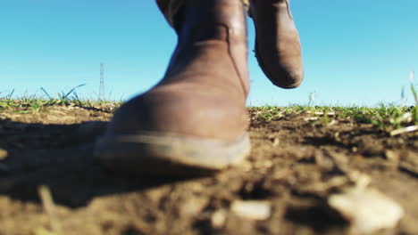 Surface-view-of-masculine-legs-and-feet-walking-towards-camera-in-muddy-grass-field