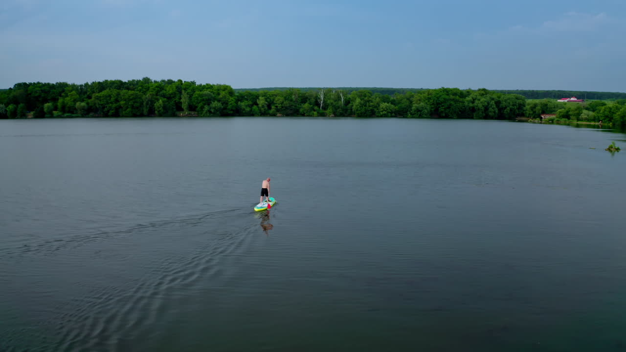 Active adventure on water. Sportsman training on water while standing on a board with oars on the background of beautiful summer landscape. Extreme sport.
