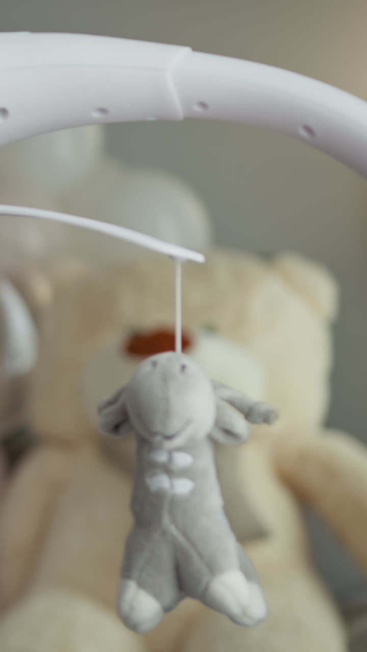 Primo piano di una giostrina per culla con morbidi giocattoli di peluche che ondeggiano delicatamente sopra un grande orsetto di peluche.
