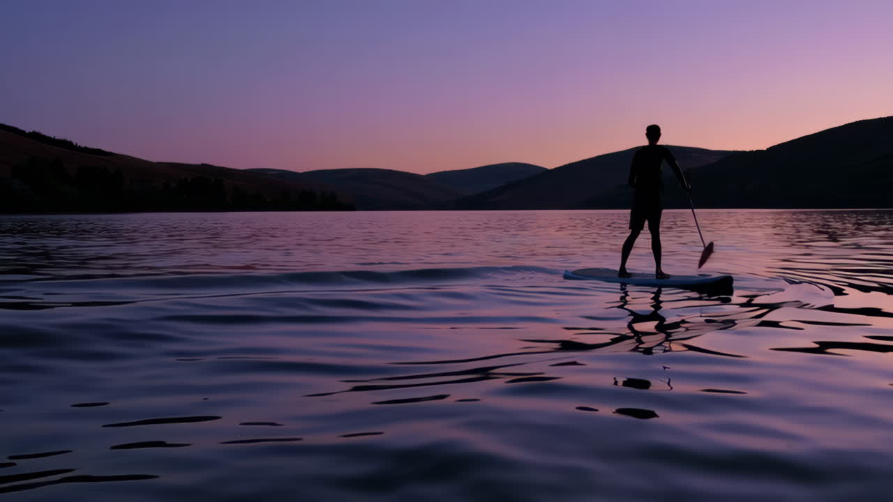 Person paddleboarding on a calm lake at twilight