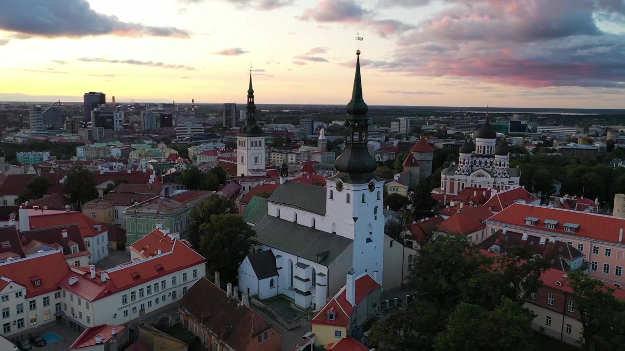 Filmato mozzafiato con drone del Centro Storico medievale di Tallinn al tramonto. L'inquadratura mostra la Collina di Toompea, la Cattedrale di Santa Maria e gli edifici dai tetti rossi sotto un cielo drammatico di nuvole rosa e arancioni.