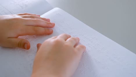 Blind-Caucasian-schoolboy-hands-reading-a-braille-book-at-desk-in-classroom-at-school-4k