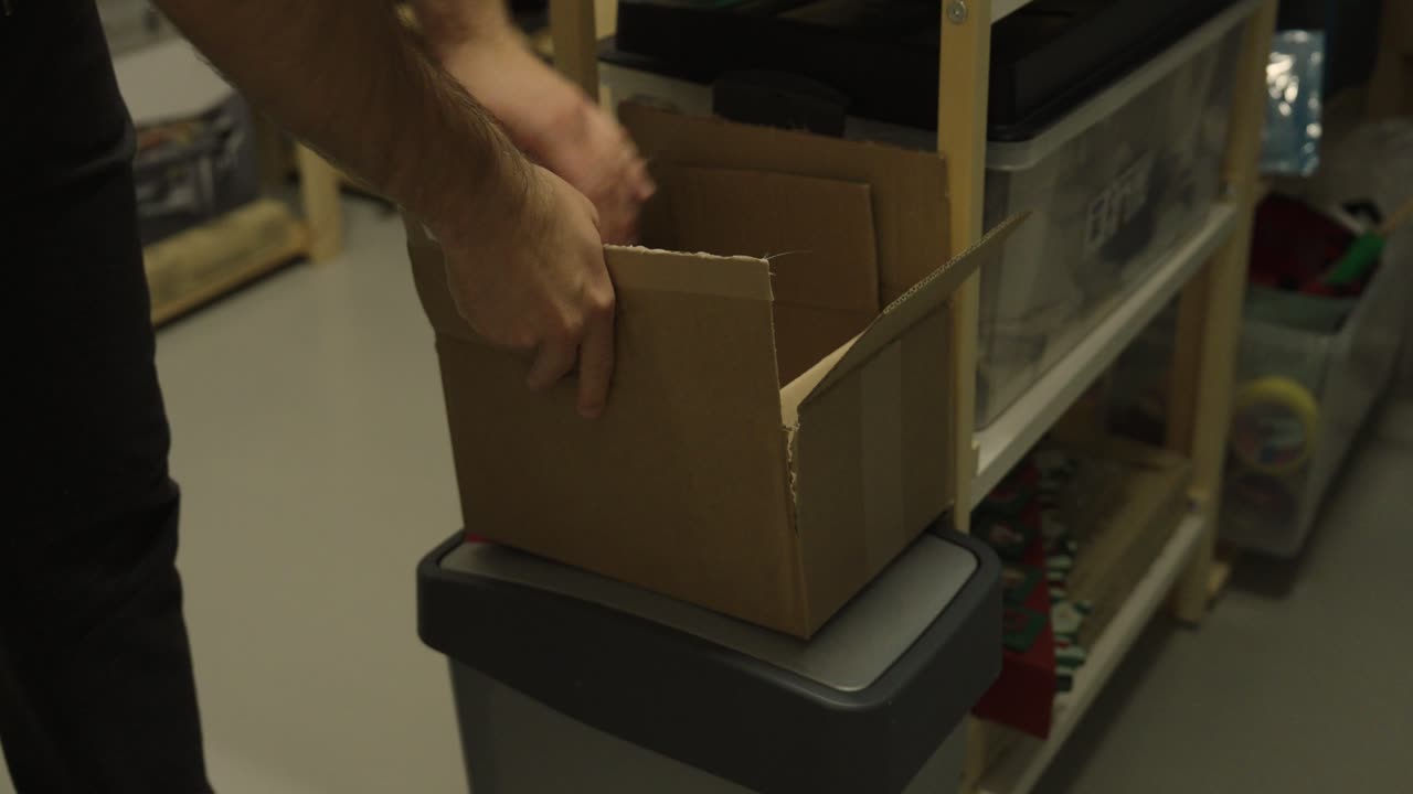 A man places smaller cardboard boxes into a larger one, symbolizing recycling, organization, or packaging in a storage area
