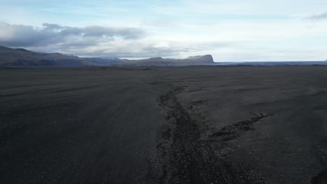 Black-sands-leading-down-to-mountains-in-the-South-of-Iceland,-aerial