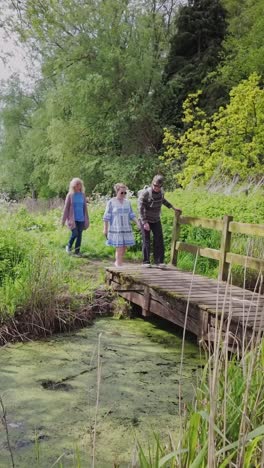 group of girlfriends cross swamp footbridge on nature trail vertical