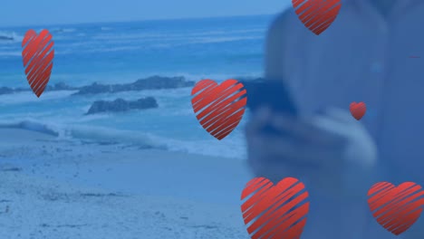 animación de corazones flotando sobre las manos de una mujer caucásica usando un teléfono inteligente
