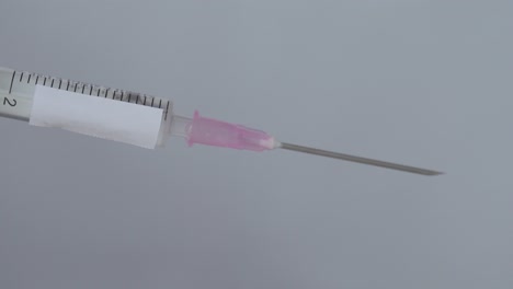 syringe for vaccination with drops on needle being flick by finger, close up