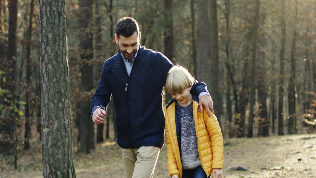 padre feliz caucásico y su pequeño hijo caminando y hablando en el bosque