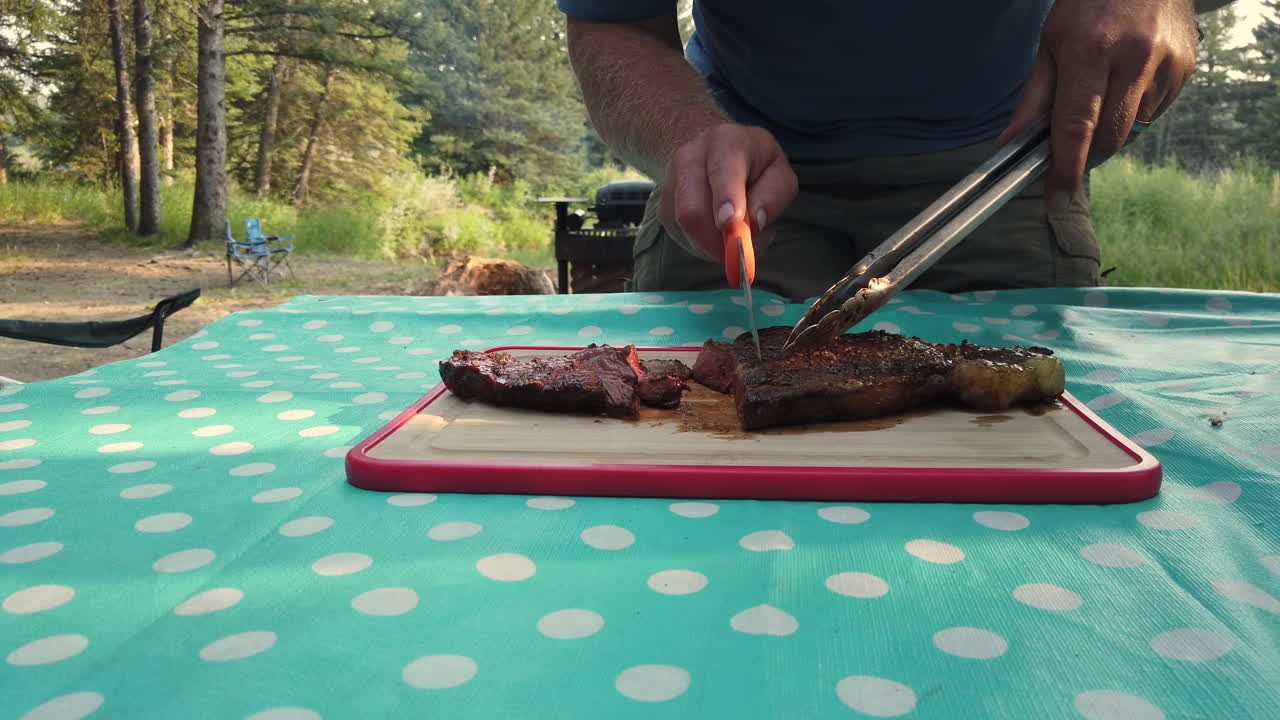 hombre cortando bistec asado en una tabla de cortar durante el viaje de campamento
