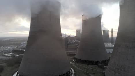 aerial dolly right view of uk power station cooling towers smoke steam emissions, sunrise reveal behind chimney