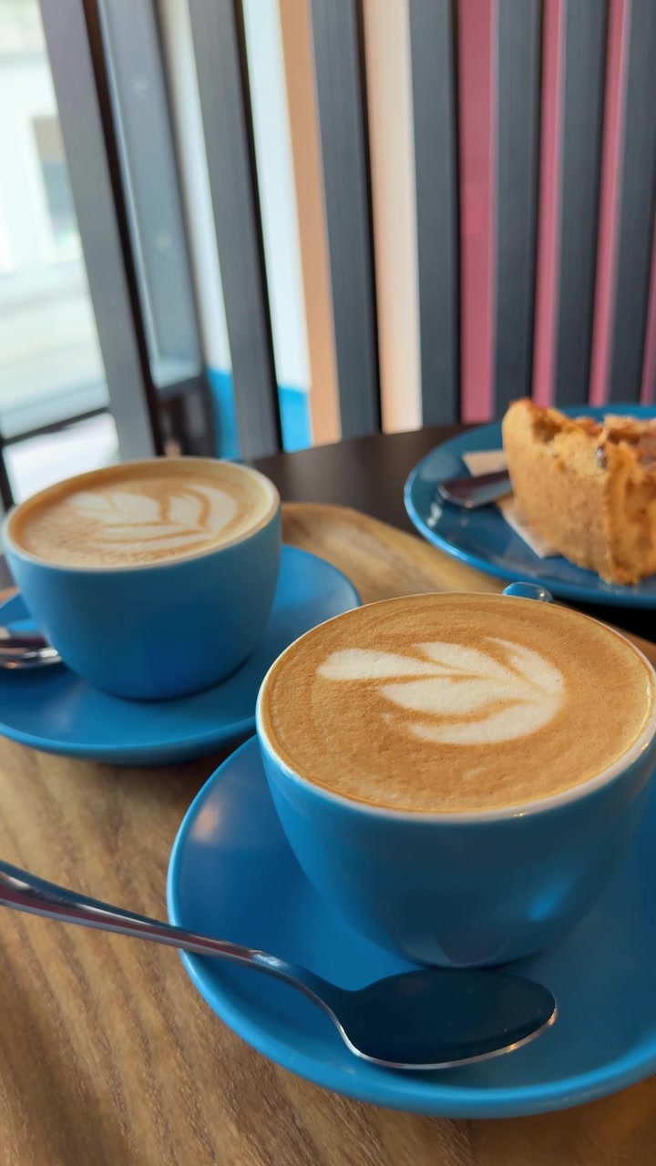 Ripresa di un vlogger di caffè e pasticcini per i social media. Filmato verticale ravvicinato di tazze di caffè latte e torta su un moderno tavolo da caffè con tazze blu in una scena accogliente di pausa caffè in stile UGC. Bevanda.
