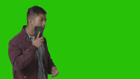 Studio-Shot-Of-Casually-Dressed-Young-Man-Talking-On-Mobile-Phone-Against-Green-Screen-