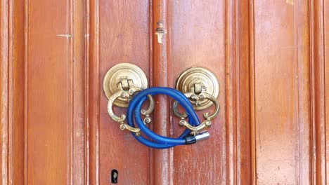 close-up of a wooden door with ornate handles and a blue padlock