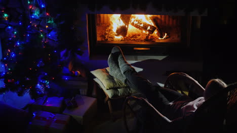 noche junto a la chimenea - una mujer joven descansando en una mecedora mirando el fuego en la chimenea