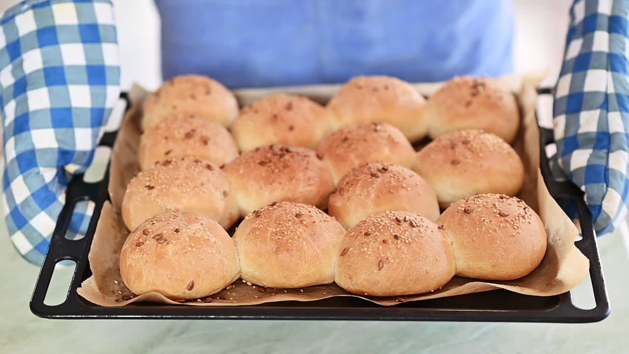 A tray of freshly baked golden burger buns sprinkled with sesame and flax seeds, just out of the oven