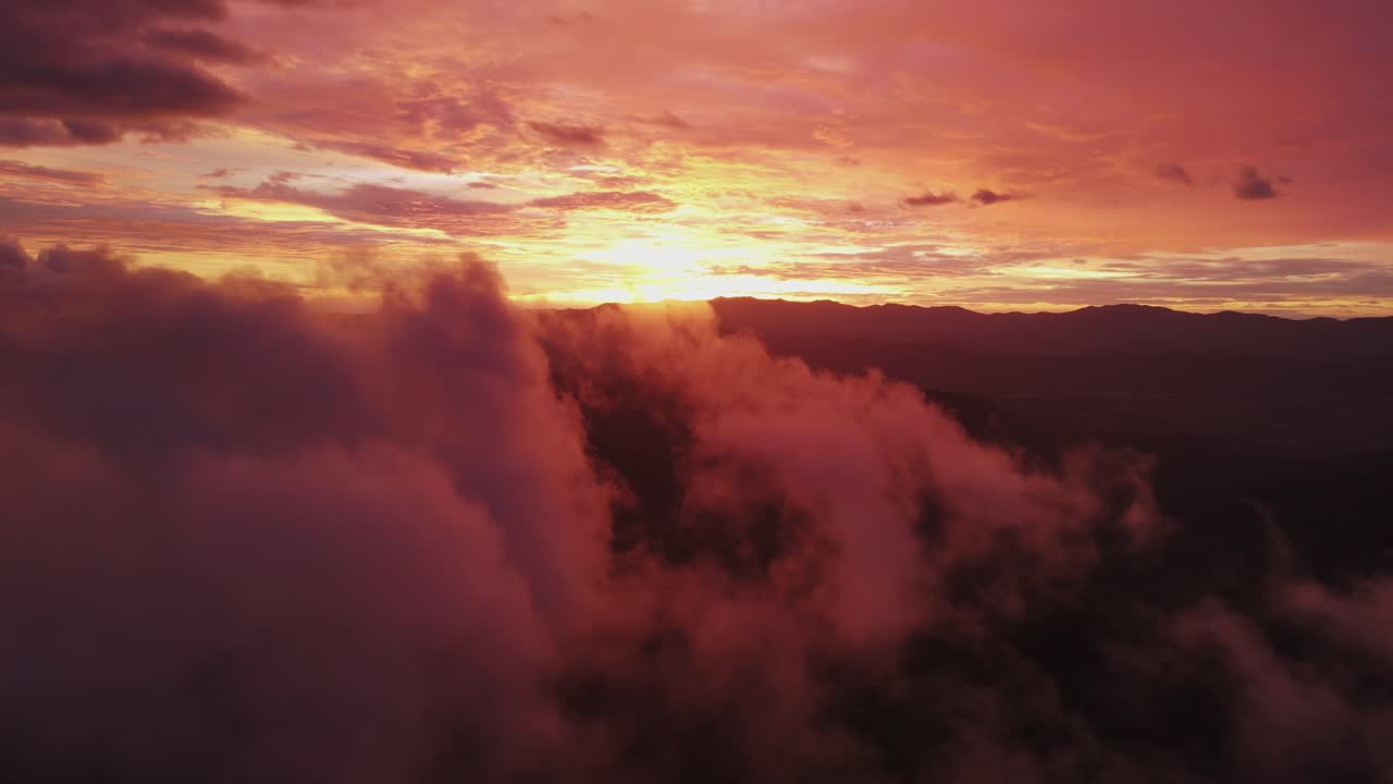 cielo rojo brillante y sol al atardecer con niebla y nubes esponjosas en primer plano, dron de 4k