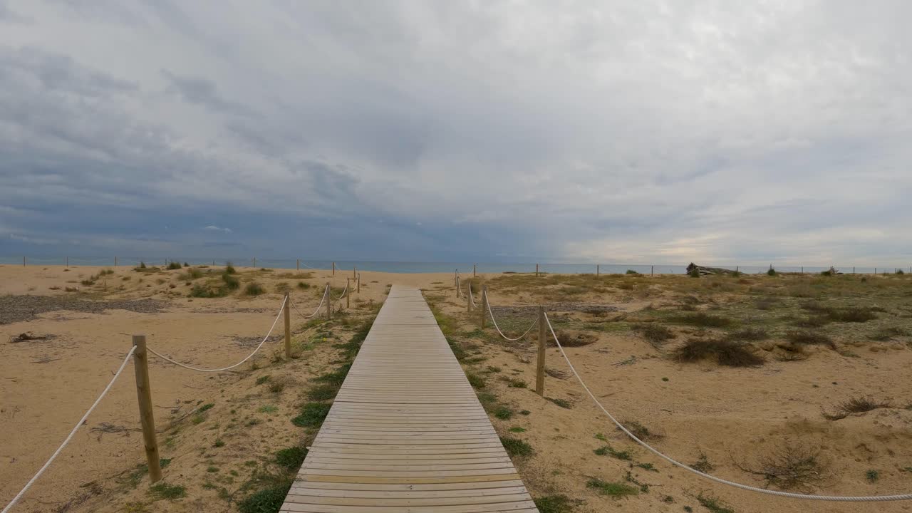 Wooden bridge over the sand direction to the beach walking in slow motion gimbal drone cloudy stormy day