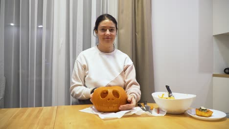 foto de una mujer joven en casa que muestra una calabaza tallada para halloween