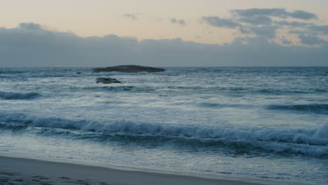 slow-motion-view-of-calm-beach-waves-splashing-genlte-on-sandy-shore-seagul-flying-in-seaside-sunset