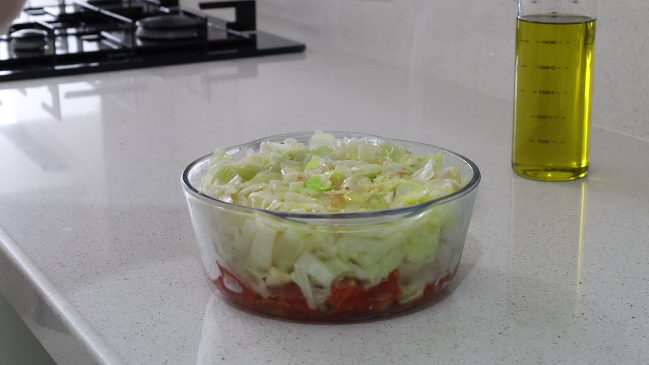 Close-up of fresh cabbage and tomato salad in a glass bowl as salt is being sprinkled on top, emphasizing preparation of healthy homemade meals