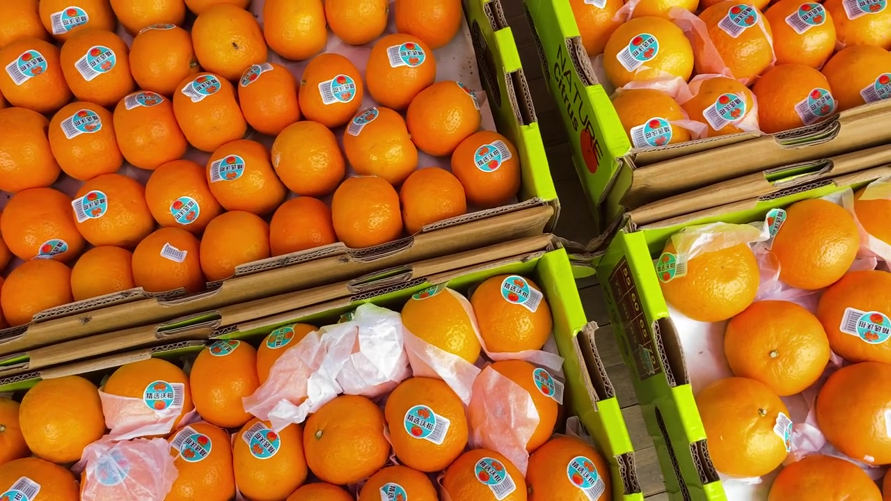 Laranjas doces enchem caixas de mercado empilhadas, muitas com adesivos e embrulho de papel