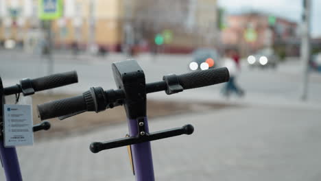 close view of purple electric scooters parked in a bustling urban area,the background includes blurred details of a cityscape with moving cars and people