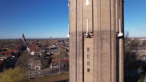 aerial closeup and reveal of former dutch brick water tower in zutphen now repurposed as a residential home with the hanseatic town in the background against a blue sky