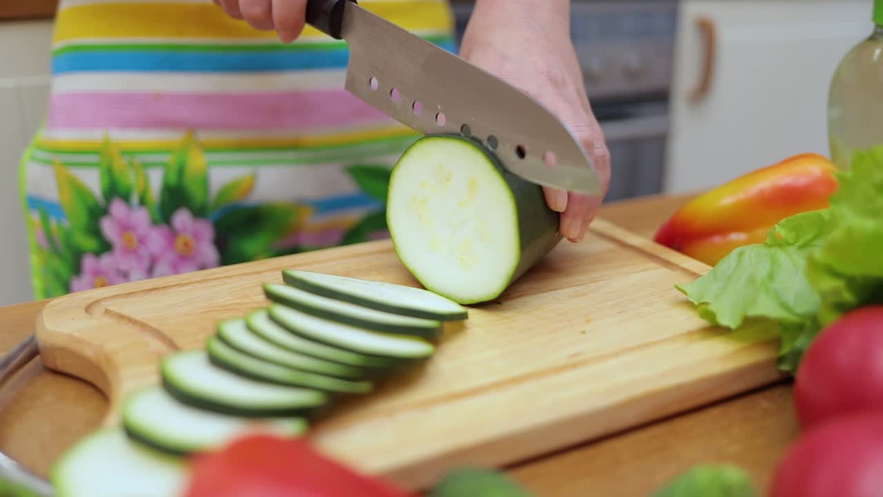 Women's hands Housewives cut with a knife fresh zucchini on the cutting Board of the kitchen table