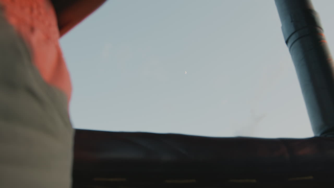 close up of glowing crescent moon beautifully framed by hot air balloon wicker edge and metal riser pipe under pastel dawn sky offering tranquil aerial moment over sprawling fields